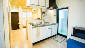 A compact kitchen with white cabinets, a stainless steel sink, and a black range hood. - Oyado Toshi (Kyoto)