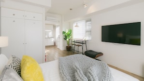 A modern bedroom with a bed, a TV, a desk, and a potted plant. - Akebono 5-D (Naha)