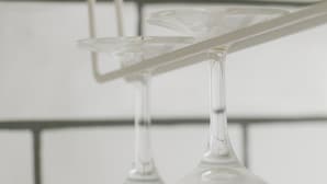 Two clear wine glasses hanging from a white, transparent holder against a white tiled wall. - Akebono 5-D (Naha)