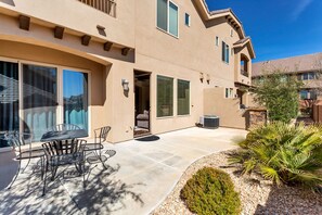 A two-story house with a patio, outdoor furniture, and a small garden.