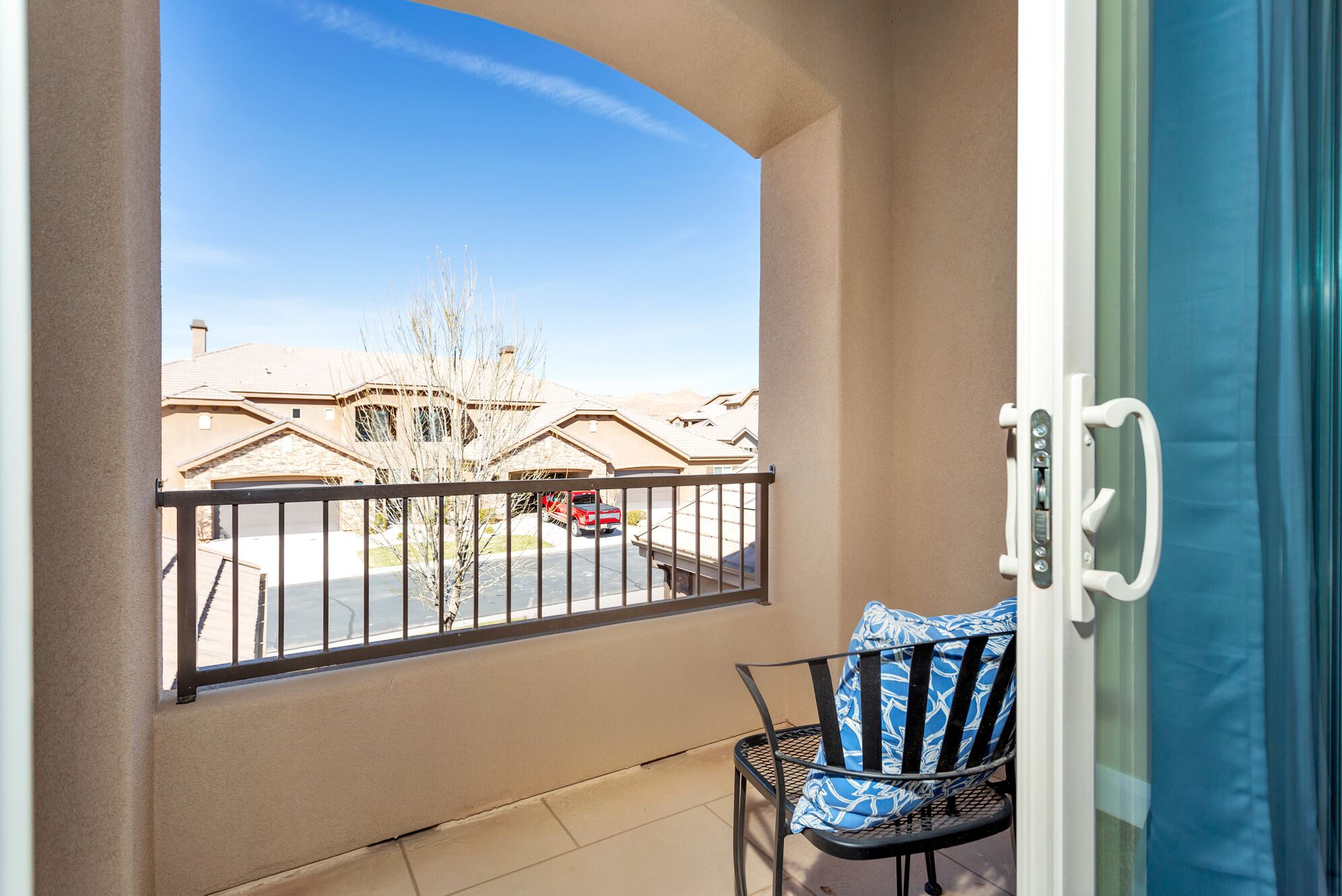 A balcony with a view of a residential area, a chair, and a door with a handle.