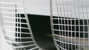 Two metal wire chairs with a black seat and a metal frame, positioned in front of a white table. - Akebono 5-C (Naha)
