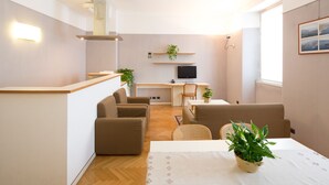 Een moderne woonkamer met een bank, een eettafel en een televisie. Achtergrond bevat planten en een houten bureau.