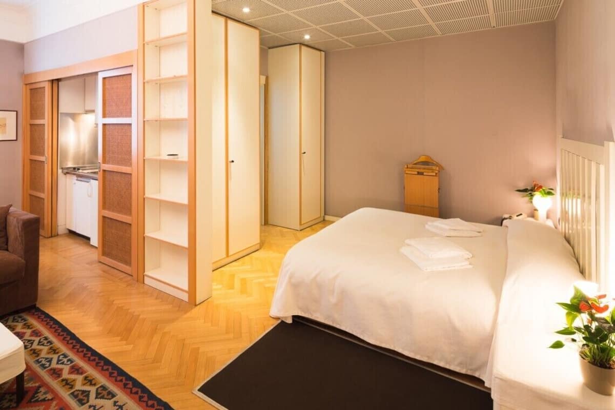 A bedroom with a bed, a wardrobe, a radiator, a potted plant, and a small table with a lamp.