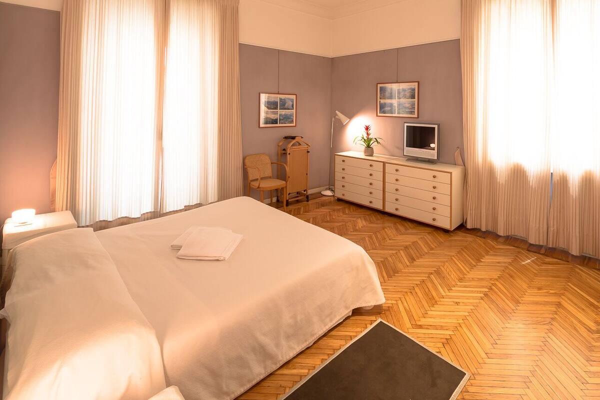 A hotel room with a large bed, a desk with a lamp, a TV, and a dresser.