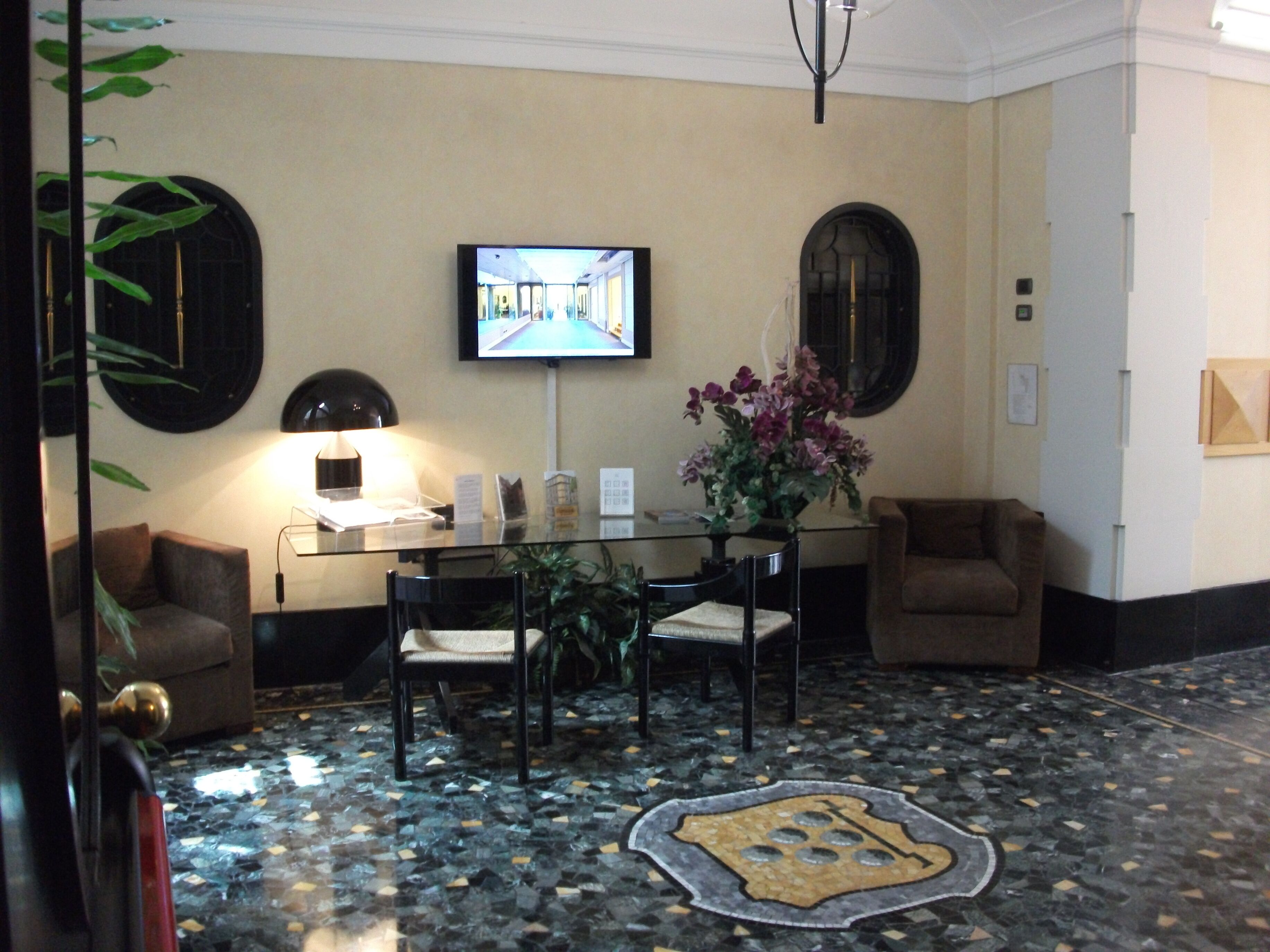 Un vestíbulo con una mesa de vidrio, sillas, televisor y una planta decorativa.