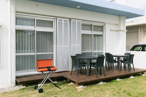 An outdoor patio with a table and chairs, a grill, and a window with shutters. - Sunset Breeze Chatan  (Chatan)