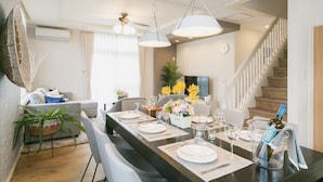 A modern dining area with a long table set for six, a sofa, and a staircase leading to an upper floor. - Sunset Breeze Chatan  (Chatan)