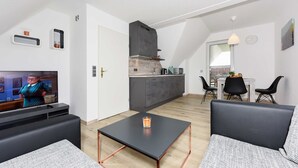 A modern living room with a flat-screen TV, a coffee table, and a sofa. There is a kitchen area with a microwave and a sink. - Vacation apartment 2 in Haus Meeresbrise Carolinensiel - Holiday apartments 2 and 3 in the (Wittmund)