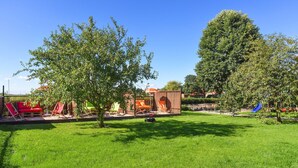 A backyard with a red sofa, orange chairs, a small brick structure, and a blue slide. - Vacation apartment 2 in Haus Meeresbrise Carolinensiel - Holiday apartments 2 and 3 in the (Wittmund)