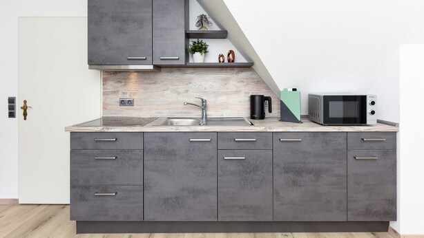 A modern kitchen with grey cabinets, a stainless steel sink, and a microwave. - Vacation apartment 2 in Haus Meeresbrise Carolinensiel - Holiday apartments 2 and 3 in the (Wittmund)