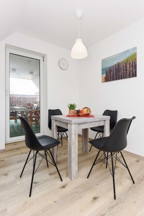A dining area with a wooden table, four black chairs, a white pendant light, a clock, and a painting on the wall.