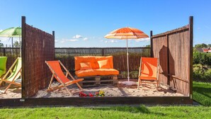 A fenced outdoor area with a sandy floor, featuring a wooden bench, two lounge chairs, and an umbrella. - Vacation apartment 2 in Haus Meeresbrise Carolinensiel - Holiday apartments 2 and 3 in the (Wittmund)