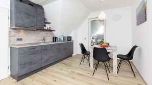 A modern kitchen with grey cabinets, a wooden countertop, and a dining area with a white table and black chairs. - Vacation apartment 2 in Haus Meeresbrise Carolinensiel - Holiday apartments 2 and 3 in the (Wittmund)