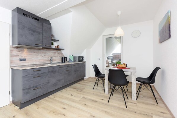 A modern kitchen with grey cabinets, a wooden countertop, and a dining area with a white table and black chairs.