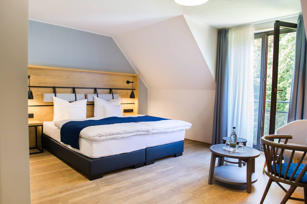 A modern hotel room with a bed, bedside table, and a small round table with a chair.