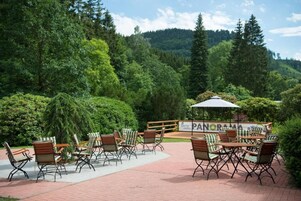 Un patio al aire libre con sillas y mesas de mimbre, rodeado de exuberante vegetación y montañas al fondo.