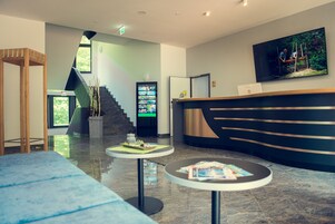 Un área de recepción moderna con una escalera, un mostrador de recepción y dos pequeñas mesas con revistas.