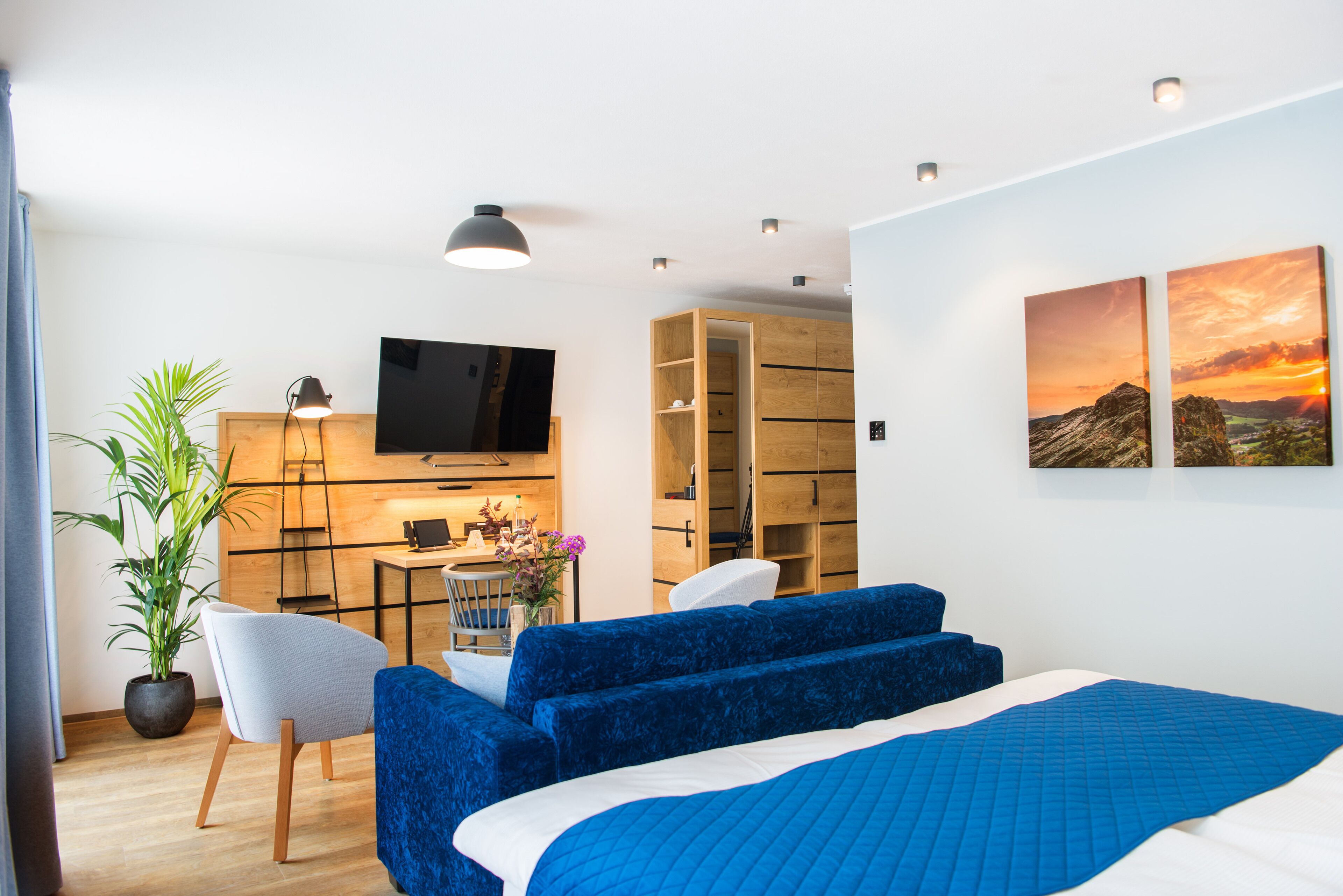 A modern hotel room with a bed, a desk with a computer, a chair, a TV, and a large window with a view.