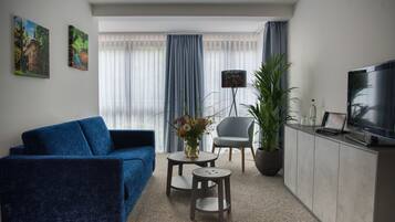 A modern living room with a blue sofa, a small coffee table, a grey armchair, a TV, and a potted plant.