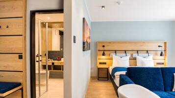 A modern hotel room with a wooden headboard, a bed with blue bedding, a white armchair, and a desk with a computer.