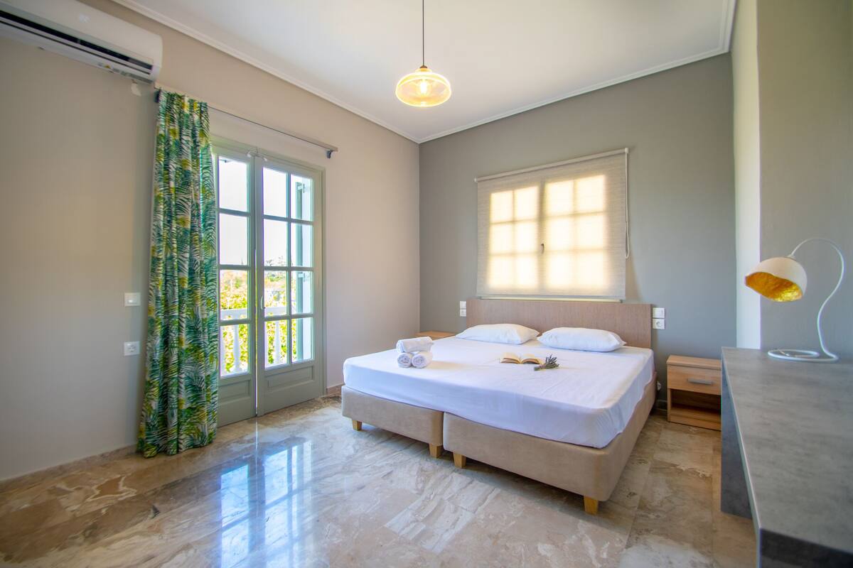 Ein Schlafzimmer mit Bett, Nachttisch, Lampe und einem Fenster mit Jalousien.