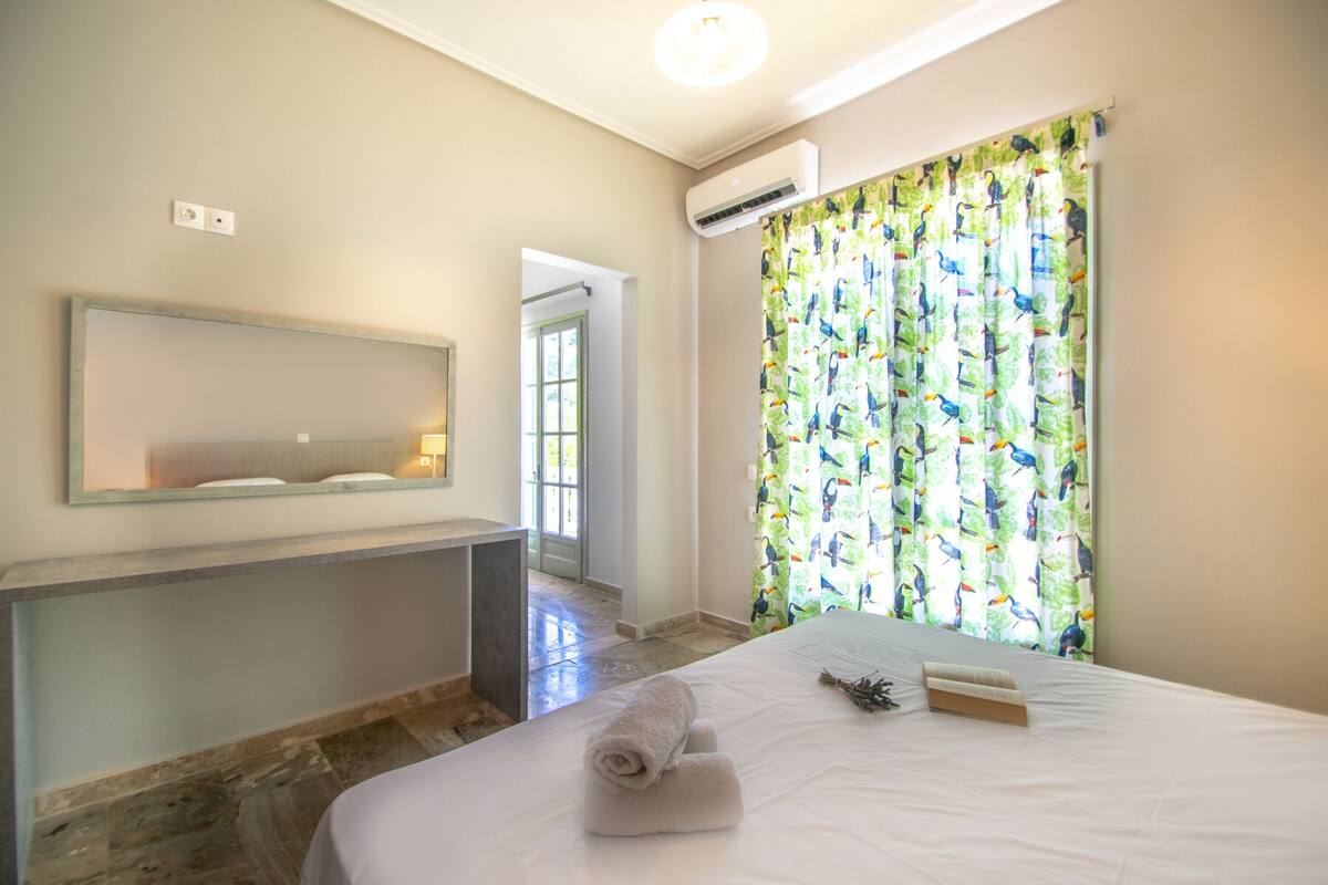 Ein Hotelzimmer mit einem Bett, einem großen Spiegel, einer Klimaanlage und einem Fenster mit bunten Vorhängen.