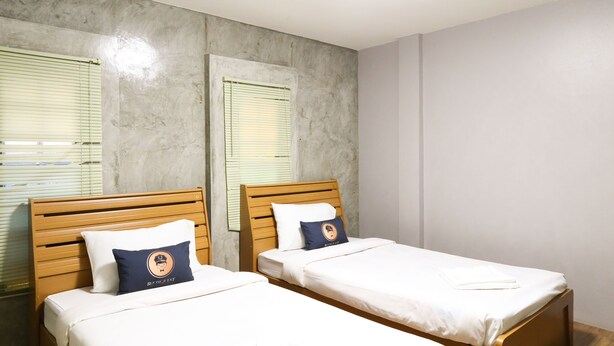 Dos camas individuales con cabeceros de madera, ropa de cama blanca y una almohada azul con un logotipo.