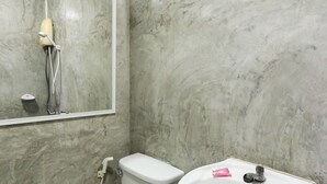 Un baño con pared de mármol, inodoro, lavamanos con espejo y ducha de mano.