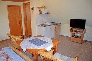 A compact room with a dining table, chairs, a small kitchenette, a television, and a door. - Vacation room under thatched roof Groot Partie - Holiday room under thatched roof in (Insel Hiddensee)
