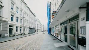 En gata med kullerstenar, vita byggnader och ett blått byggställningsställ.