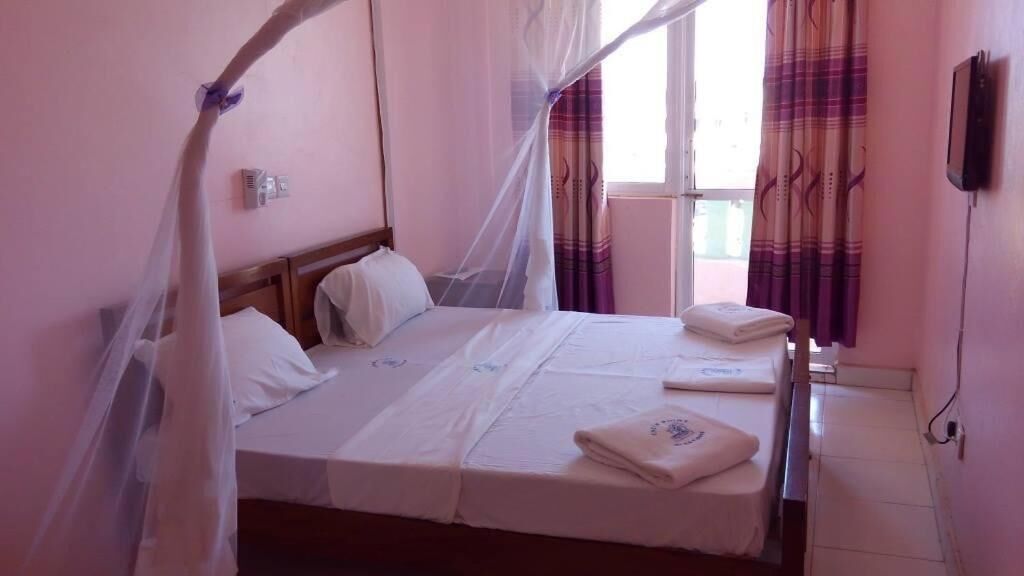 Un letto singolo con baldacchino, un comodino, un condizionatore d'aria a parete e una finestra con tende.