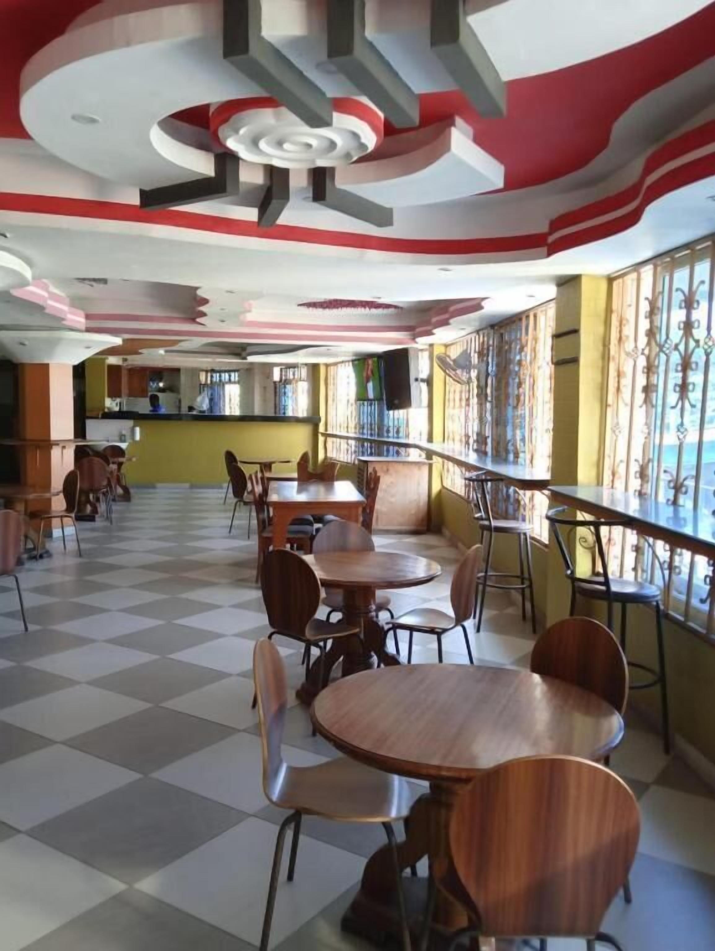 A restaurant with checkered flooring, wooden tables and chairs, and a red and white ceiling design.