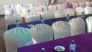 A conference room with rows of tables, each covered with a purple tablecloth and white chairs. Water bottles are placed on the tables. - Checkpoint Inn (Mombasa)