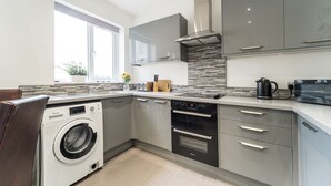 Une cuisine moderne avec des meubles gris, un four encastré et un lave-linge.