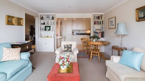 Un salon avec un canapé, une table basse ornée de fleurs, un coin repas avec une table et des chaises, et une cuisine en arrière-plan.