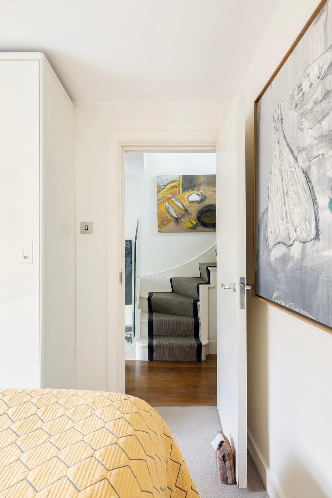 A bedroom with a bed, a painting, and a staircase leading to a dining area.