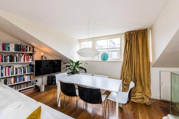 Un appartement moderne de style « loft », comprenant un coin repas, une bibliothèque et un téléviseur.