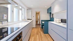 A modern kitchen with white cabinetry, a wooden floor, and a view into the dining area.