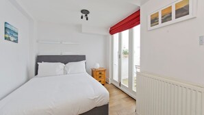 A bedroom with a bed, a nightstand, a window with red curtains, and a view of the outside.