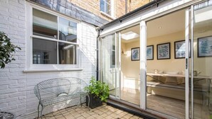 Eine Terrasse mit einem Metallstuhl, einem Blumentopf und einer Glasglastür, die zu einem Innenraum mit Tisch und Stühlen führt.