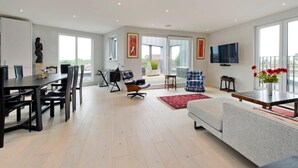 A spacious living area with a dining table, chairs, a sofa, a TV, and artwork on the walls. - Fabulous 2-bed Penthouse, Wimbledon (London)