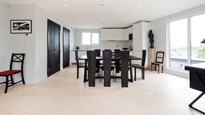 A modern kitchen with white cabinets, a dining table with chairs, and a large window providing a view of the city. - Fabulous 2-bed Penthouse, Wimbledon (London)