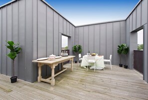 A covered outdoor patio with a wooden table and chairs, surrounded by grey walls and potted plants. - Fabulous 2-bed Penthouse, Wimbledon (London)