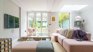 A modern living room with a glass coffee table, a pink sofa, and a large window. - Fantastic 4 Bed House in Iconic Camden (London)