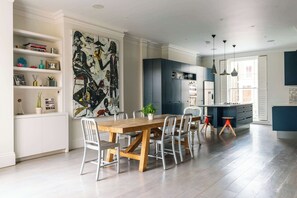 A modern kitchen with a wooden dining table, white chairs, and a large abstract painting on the wall.