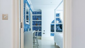 A bedroom with a bed, a desk, and a chair. There is a shelf with decorative items and a window. - Fantastic 4 Bed House in Iconic Camden (London)
