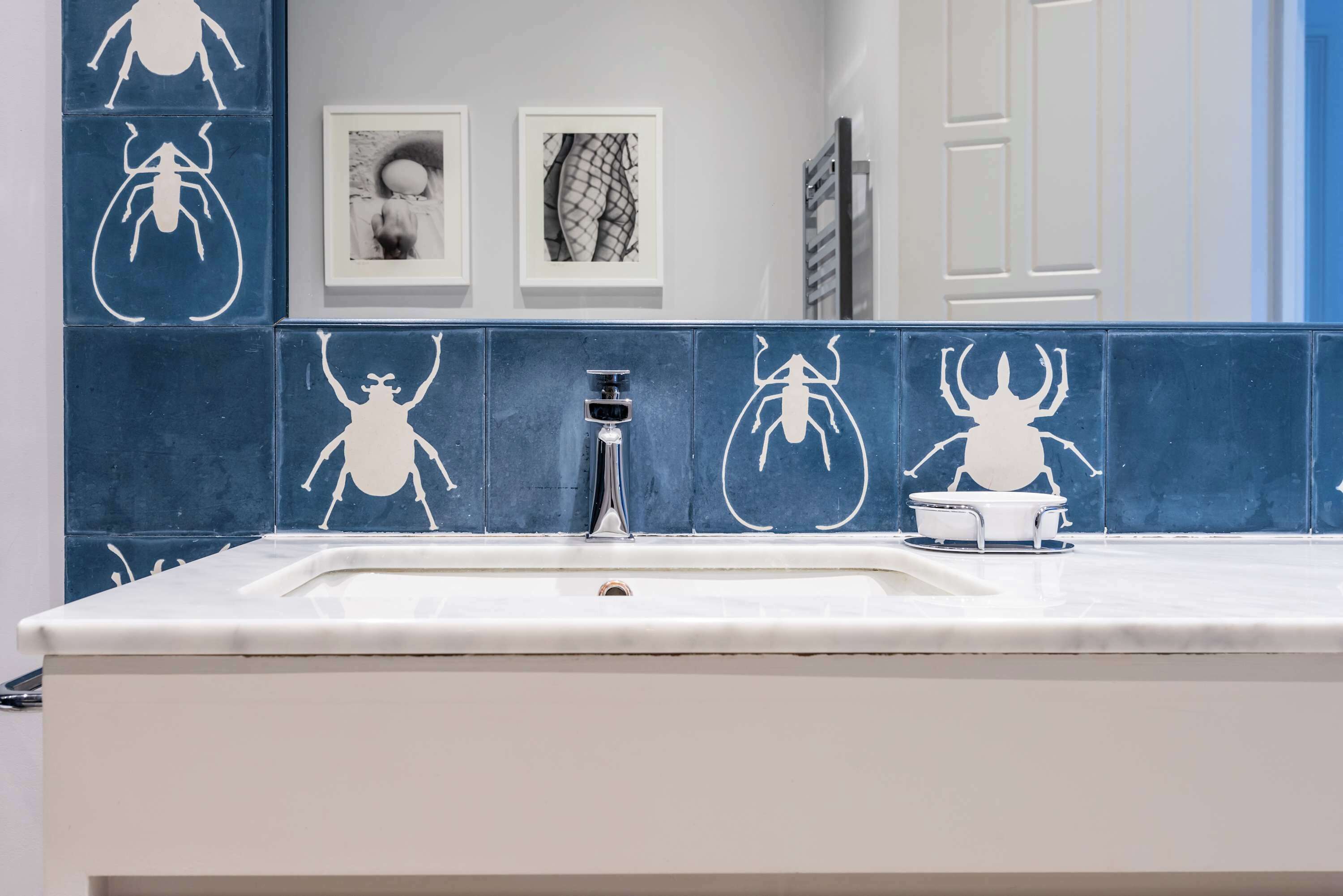 A bathroom with a sink, a mirror, and blue tiles with insect designs.