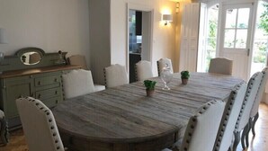Een eetruimte met een houten tafel, witte gestoffeerde stoelen en een kleine potplant.
