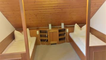Ein kleiner, gemütlicher Raum mit zwei Einzelbetten, einem Holzschrank und einem Schreibtisch mit Stuhl.